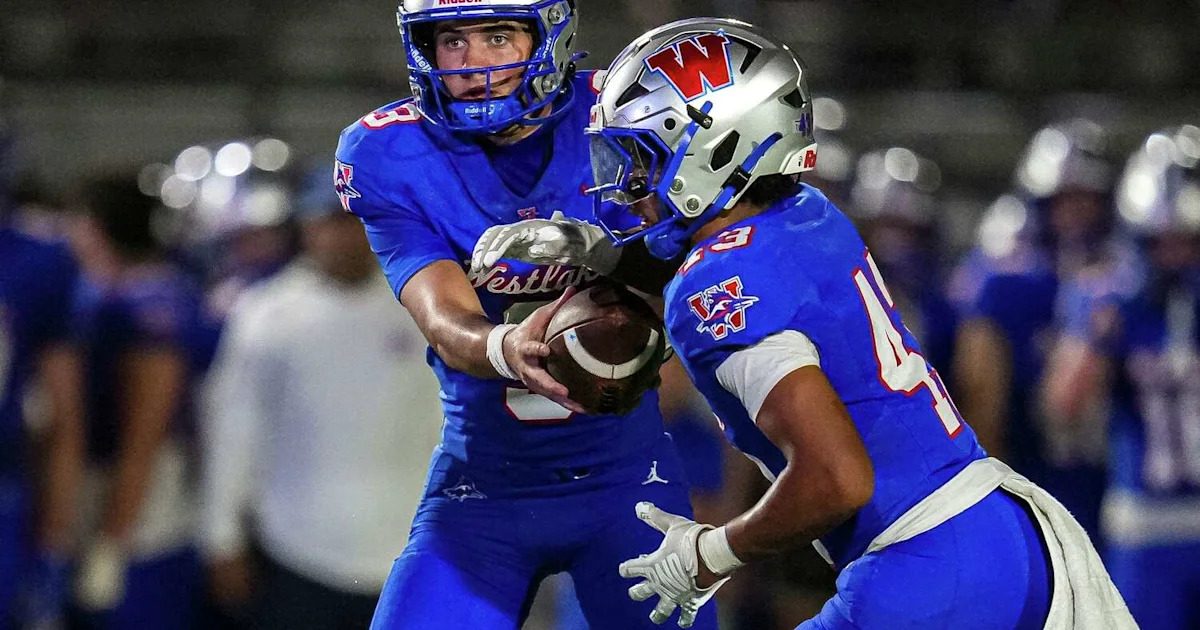Westlake and Round Rock high school football players line up at the scrimmage line under stadium lights