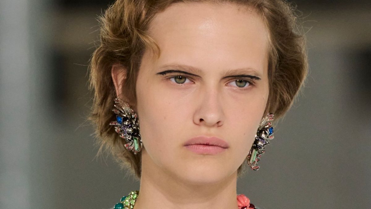 Model walking a Paris runway with blunt bangs and bold red lipstick